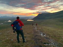Image: Mountain Rescue volunteer watches a fiery sunset across a rugged landscape.