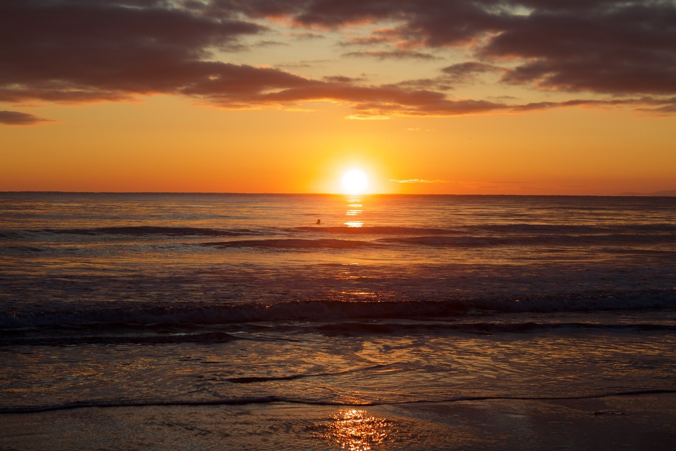 Glowing sunset lights up a lone swimmer pushing through the waves of a wide open ocean.