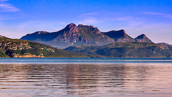 Image: Distant craggy mountain is reflected on rippling loch in foreground.