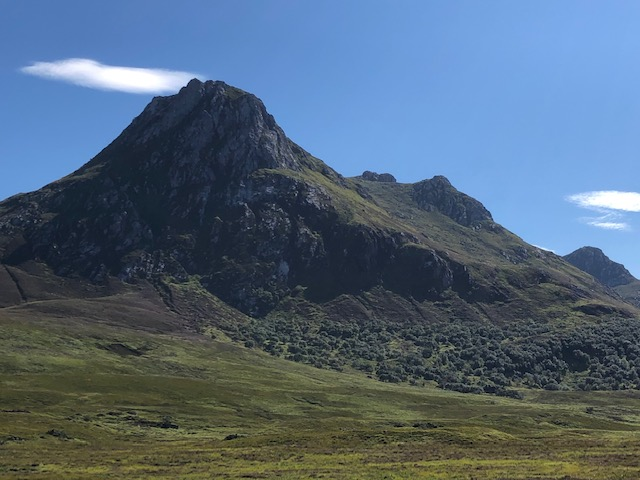 Image: Distant craggy mountain stands proud against a vibrant sky with gentle puffy clouds around it.