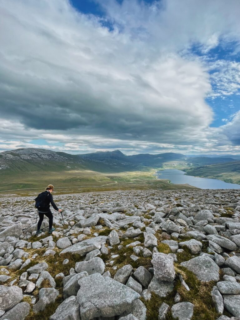 A hillwalker on Quinag walking over a boulder field, overlooking Loch Assynt in the Scottish Highlands. 