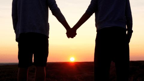 A couple holding hands romantically in front of a sunset