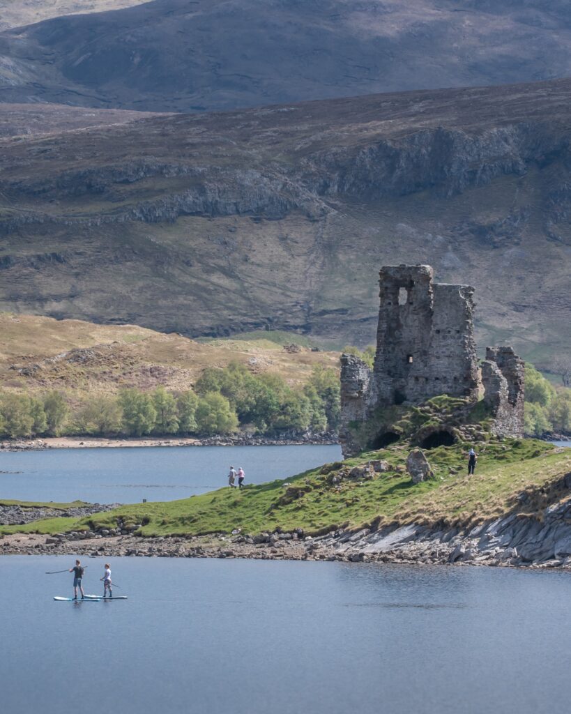 Ardvreck Castle with the lake and two people on the water. Located in Sutherland, Scotland.