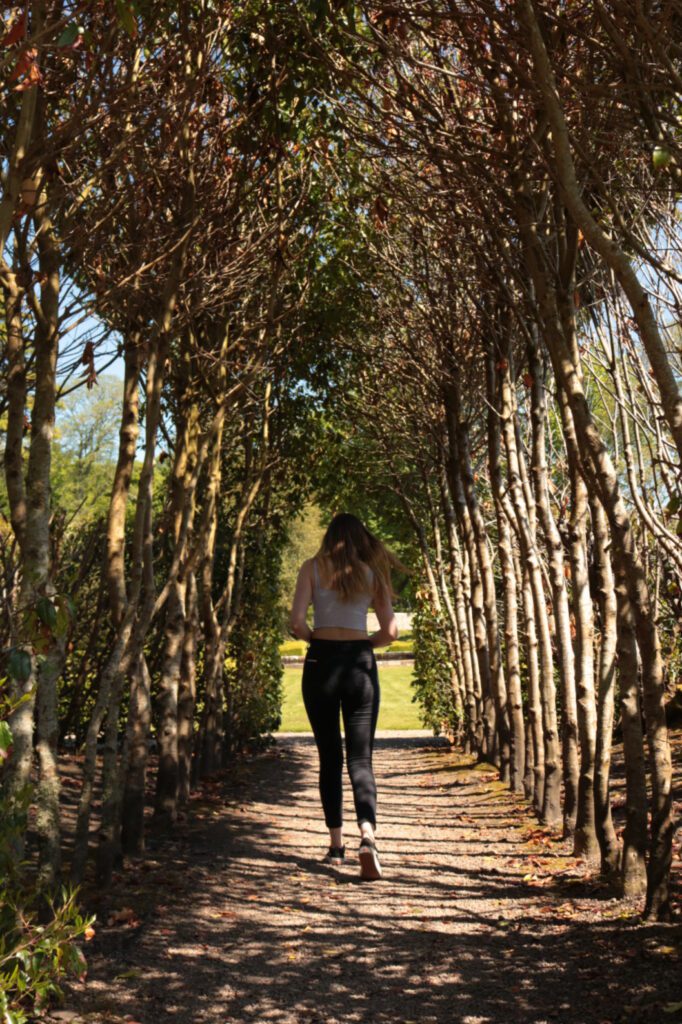 A woman walks through an archway of trees in Dunrobin Castle Gardens, Sutherland, Scotland.
