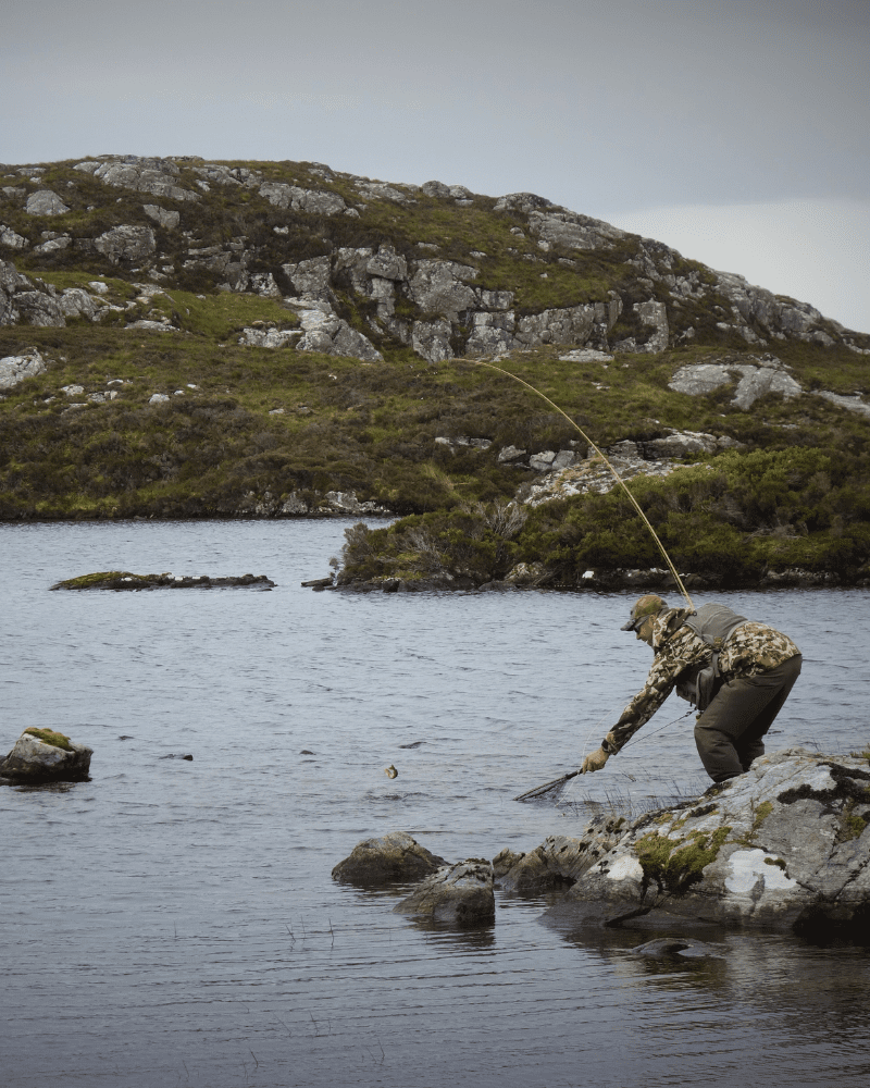 A mean reaches into a lake pulling his catch out of the water at Assynt, Sutherland, Scotland. Activities and sport in the North Highlands