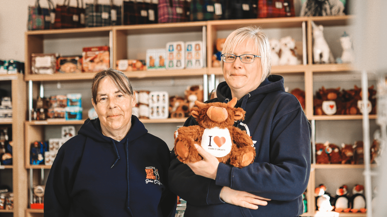 Two workers at The Groatie Buckie Gift Shop in John O'Groats, one woman is heloding a cuddly highland cow toy.