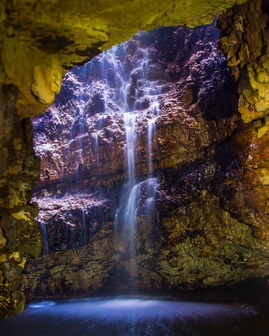 An internal view of Smoo Cave in Sutherland, Scotland. Water falls down over a moss covered cave wall. Attractions and landmarks.