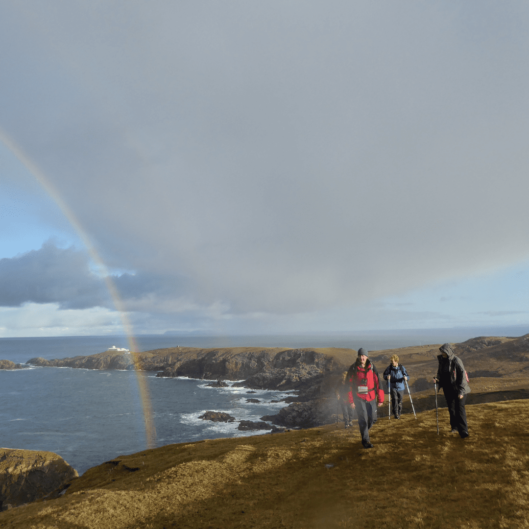 A group taking a walk near the cliffs at Strathy. A rainbow shines above them. Strathy, Sutherland, North Highlands.