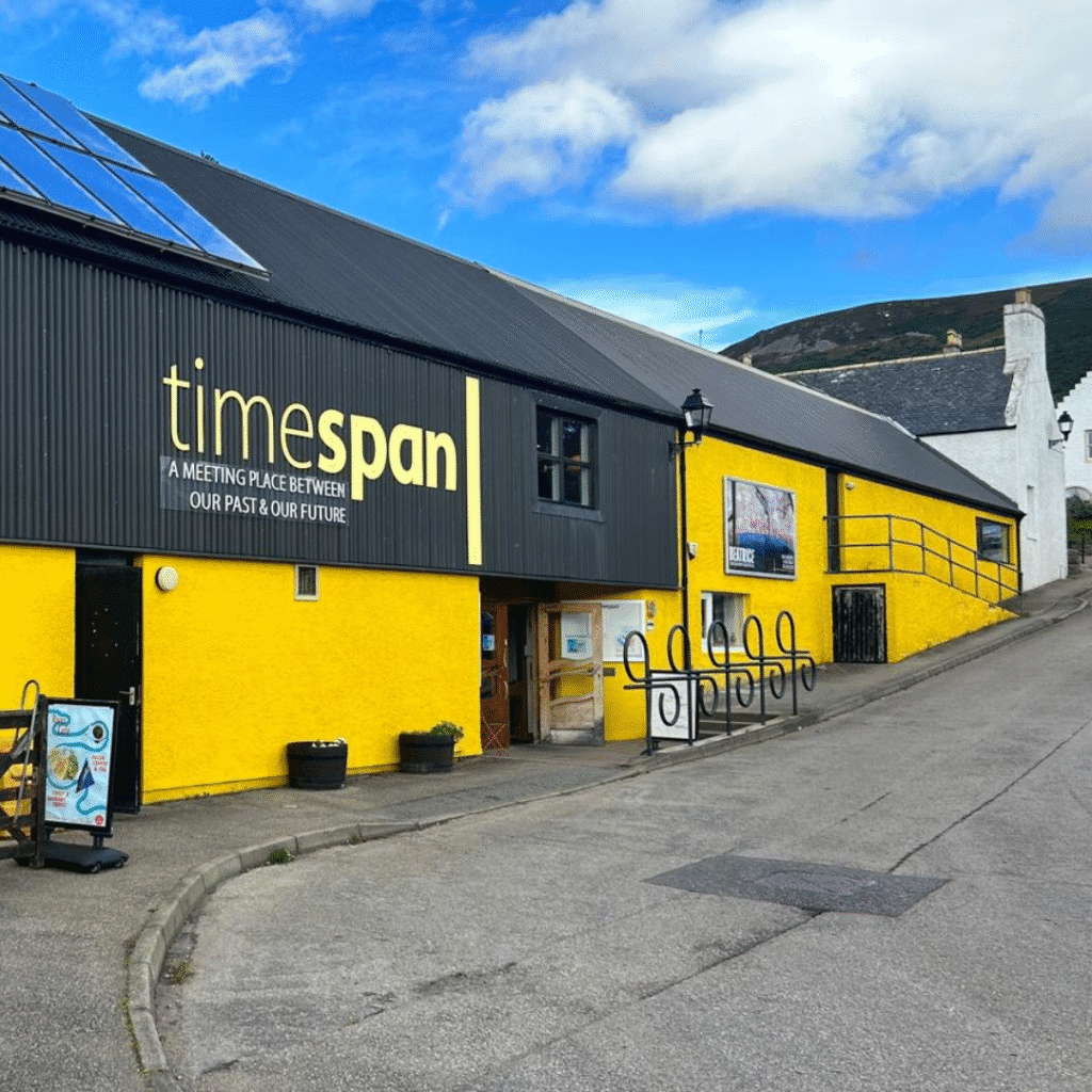 The outside of Timespan, Helmsdale, Sutherland, Scotland. A yellow and bacl building.