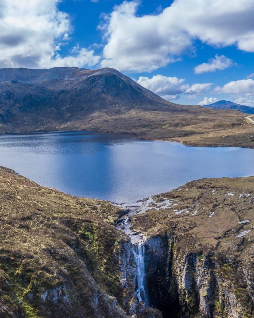 A large lake that goes into a waterfall, with a large hill in the background and beautiful blue skies, Wailing Widow Falls, nature and outdoors in the North Highlands