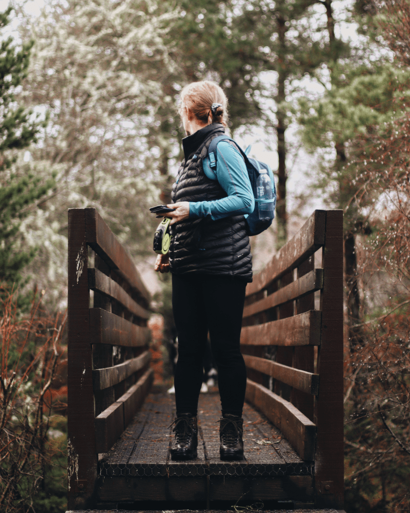 A woman stands on a bridge in a forest, looking behind her over her shoulder. In Invershin, Sutherland Scotland.