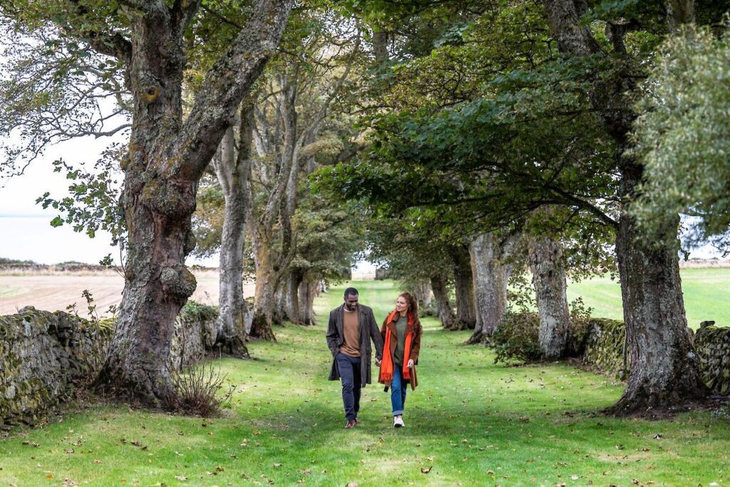 A couple walk along a path lined with trees at Glenmorangie House, near the North Coast 500