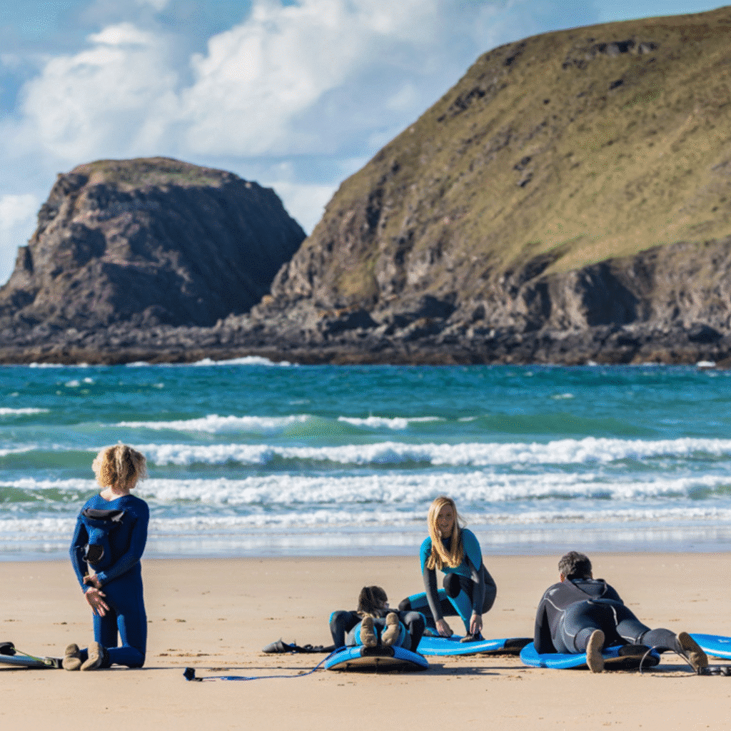 Four Surfers are sat on the beach, beautiful hills can be seen in the background. Activities and sport in the North Highlands