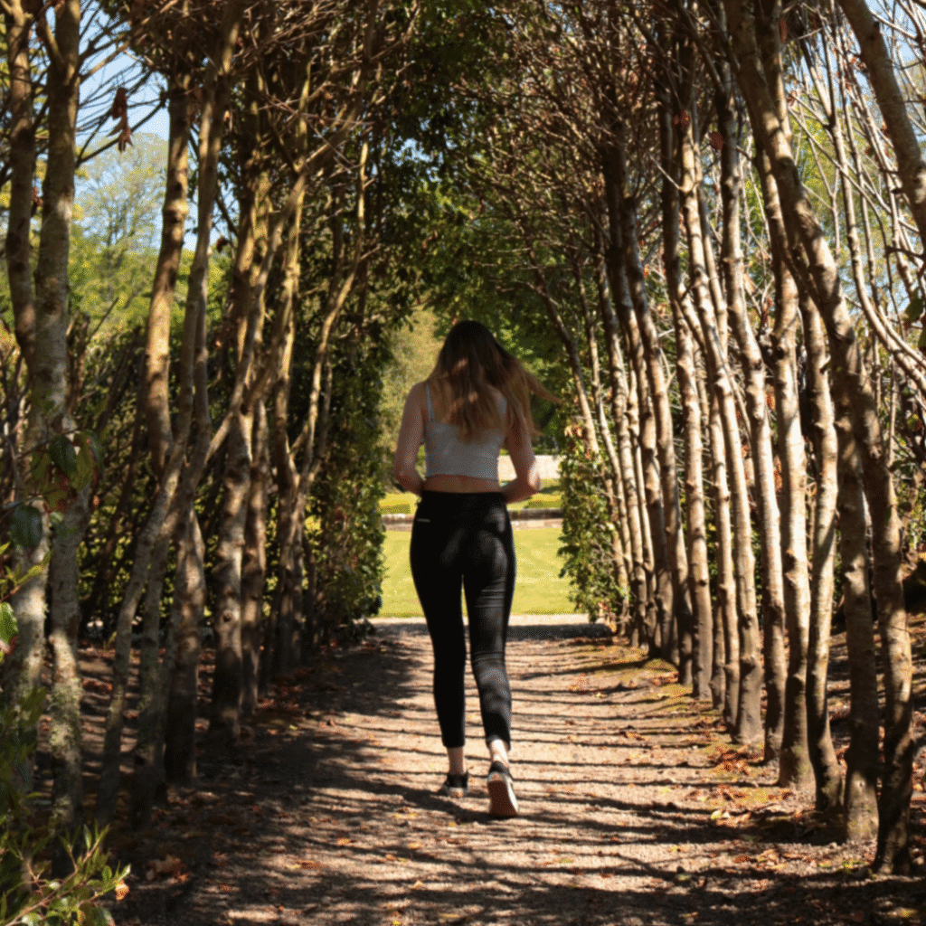 A woman walks through an archway of trees in Dunrobin Castle Gardens, Sutherland, Scotland. Attractions and landmarks.