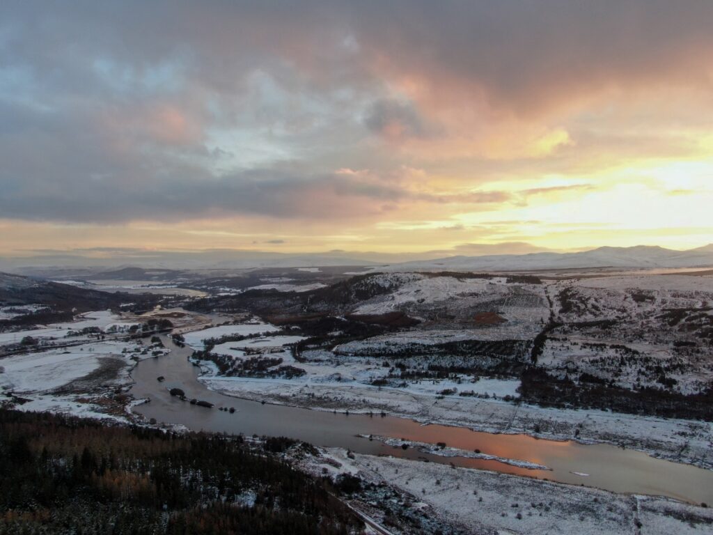 Snow-covered Kyle of Sutherland tidal estuary at sunrise, with rivers converging and golden reflections near Bonar Bridge in the Scottish Highlands.