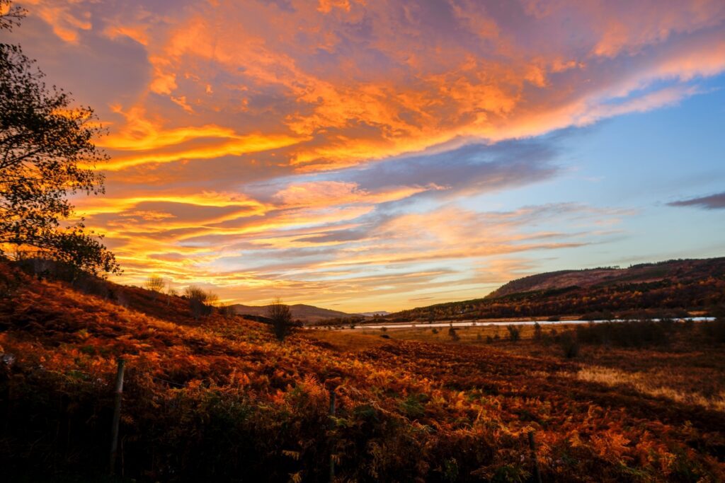 Vibrant orange golden sunset over rolling hills and autumn foliage in Sutherland.