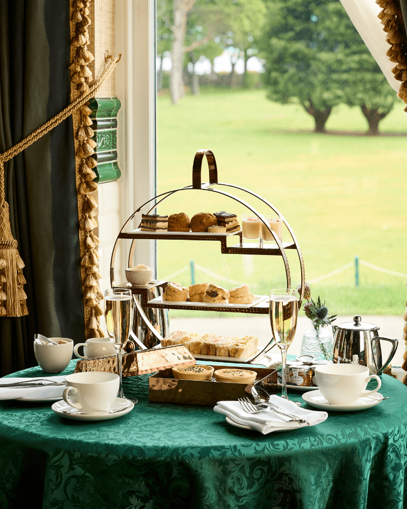 A table with green tablecloth, with a display of cakes and tea, in Dornoch Station, Sutherland, Scotland.