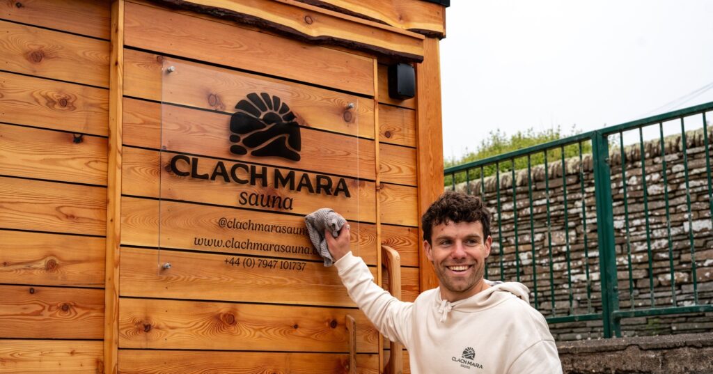 A man cleaning the glass sign on the Clach Mara Sauna