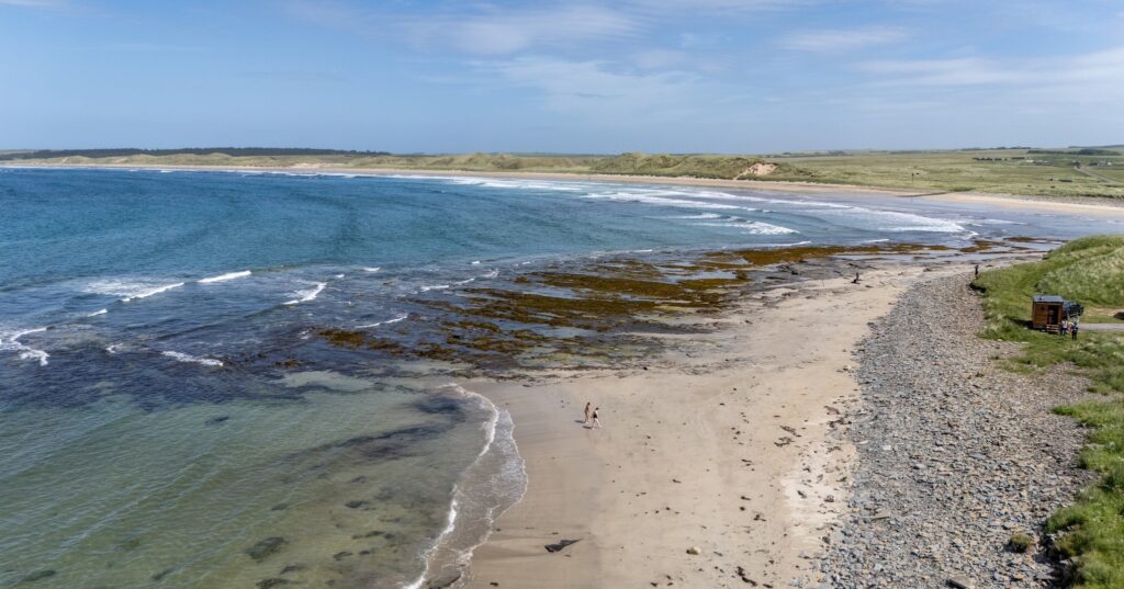 An aerial view of Castletown beach, people enjoying the beach along the north coast, with the Mara Clach Sauna for their wellness afterwards, in the North Highlands