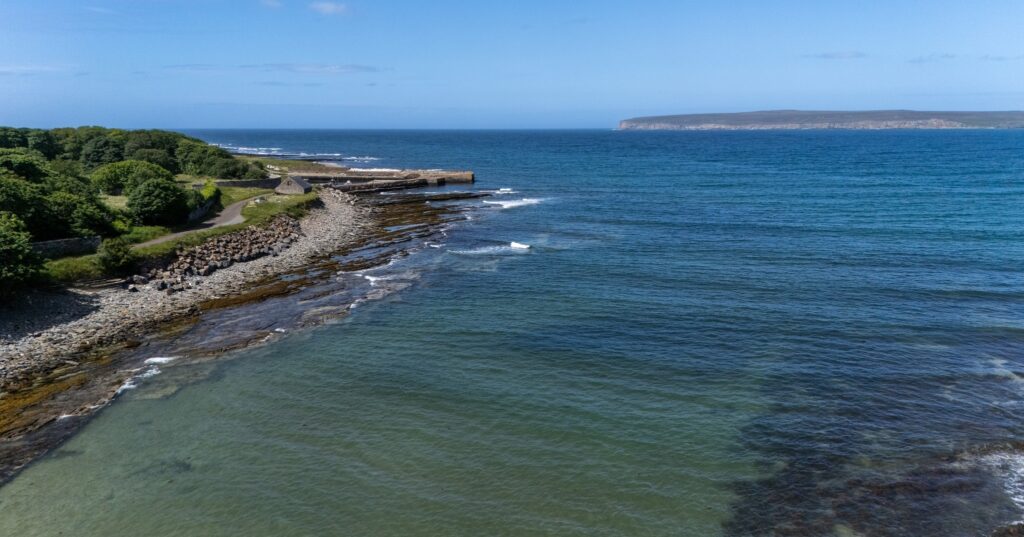 A view of Castletown Beach, clear waters with the sand and the trees along the edge, in Caithness, Scotland
