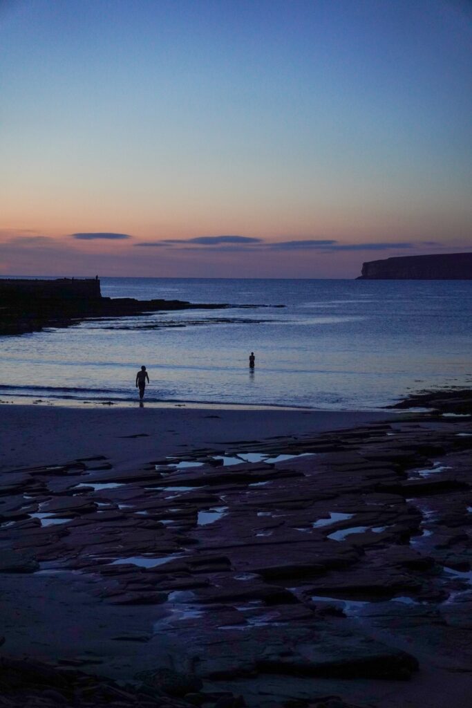 Two people running into the sea at Castletown beach at sunset, in the North Highlands