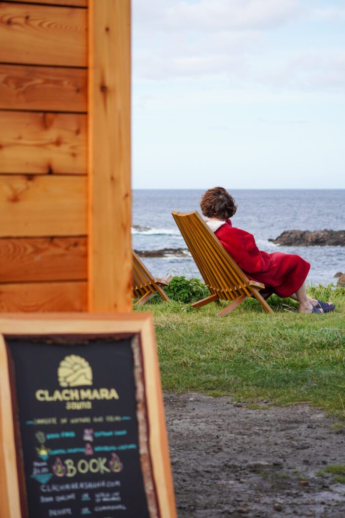 A woman sitting on a wooden recliner seat beside the beach in the North Highlands