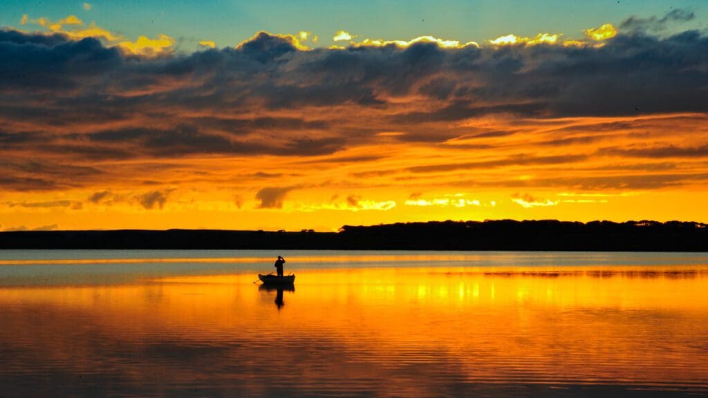 A fisherman in a rowing boat on a Highland Loch at sunset.