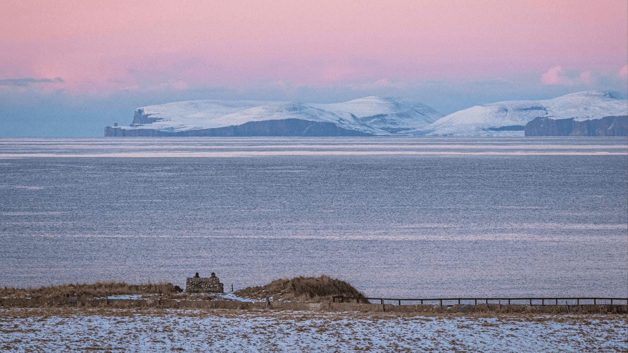 Couple sitting on a bench looking out over the Pentland from Thurso beach during winter at sunset.