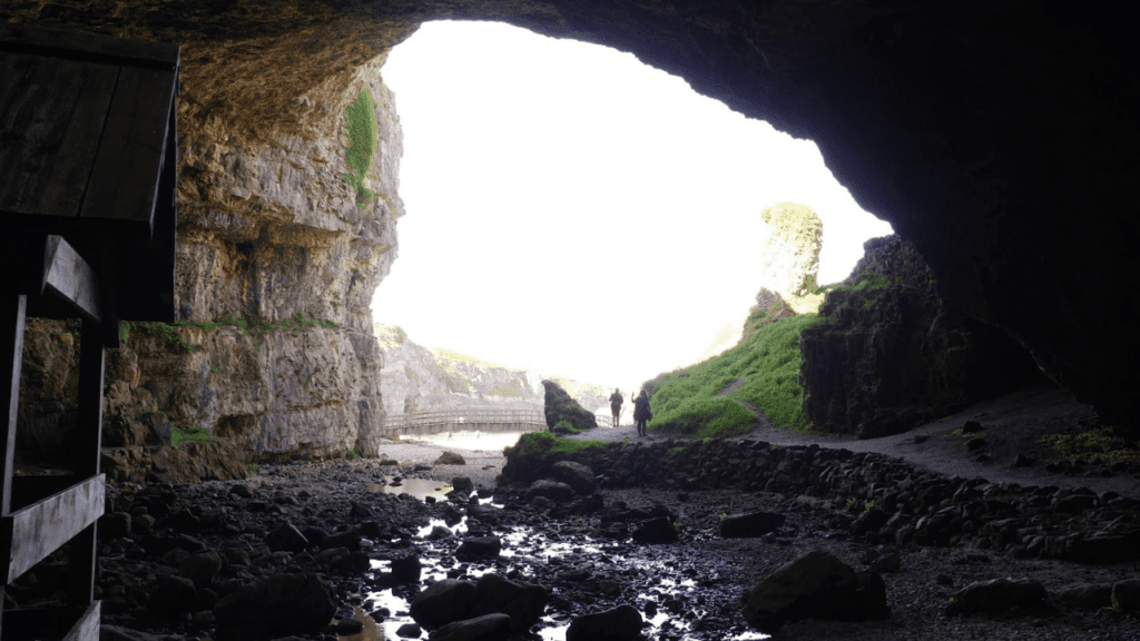 Two people stand in the entrance of Smoo Caves, the cave walls either side, Sutherland, North Highland