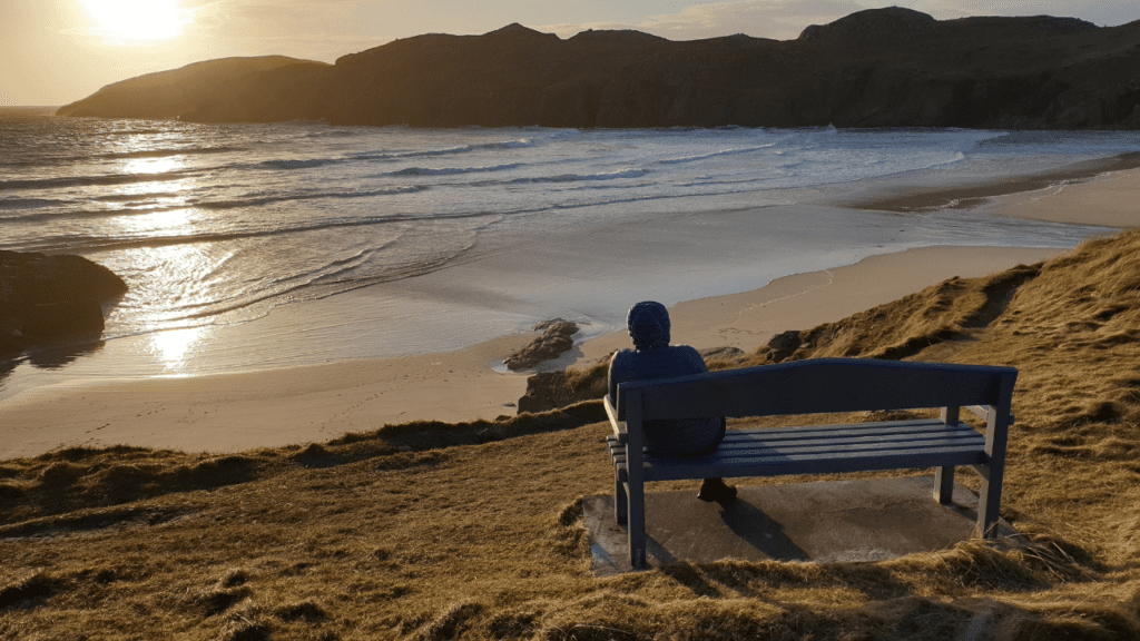 A man sitting on a bench overlooking Polin Beach at sunset, Sutherland, North Highlands
