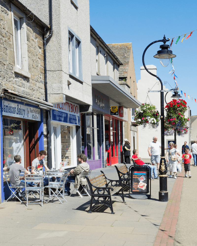 People sitting outside a bakery in the sun on Thurso High Street, Caithness, North Highland