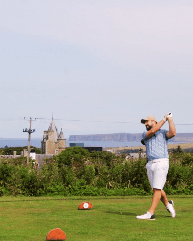 A man mid-swing at Thurso Golf course, the town can be seen in the background